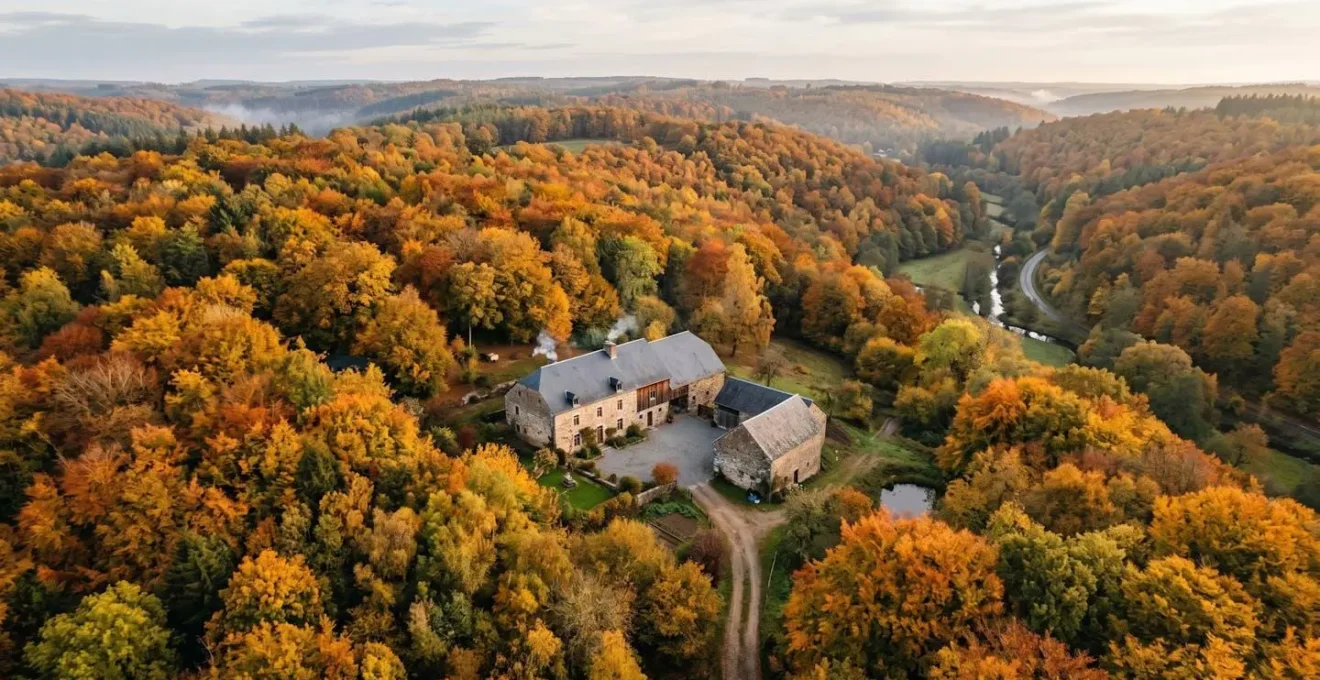 Vue panoramique d'une maison de campagne ardennaise entourée de forêts en automne, symbole de résidence secondaire en Belgique