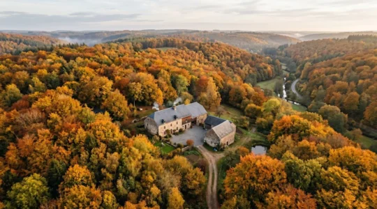Vue panoramique d'une maison de campagne ardennaise entourée de forêts en automne, symbole de résidence secondaire en Belgique